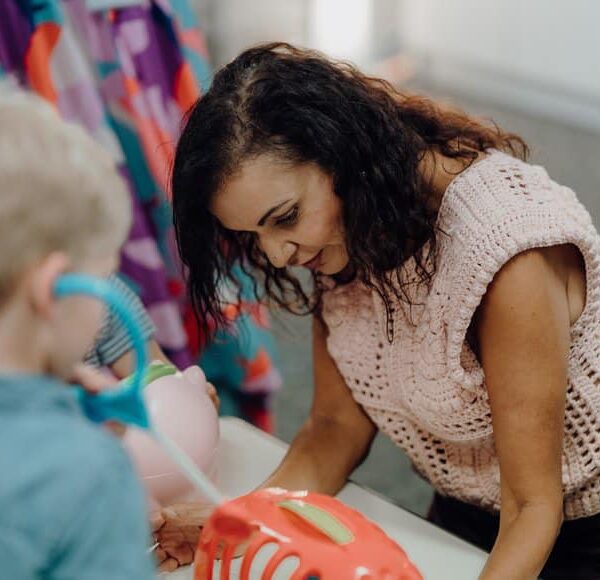 Federal Minster for Early Childhood Education, Dr Anne Aly, is pictured in play with a young blonde child who has their back to the camera.