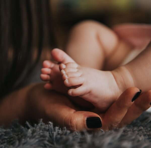 Image shows an adult hand, with dark nail polish, cradling the feet of a small child.