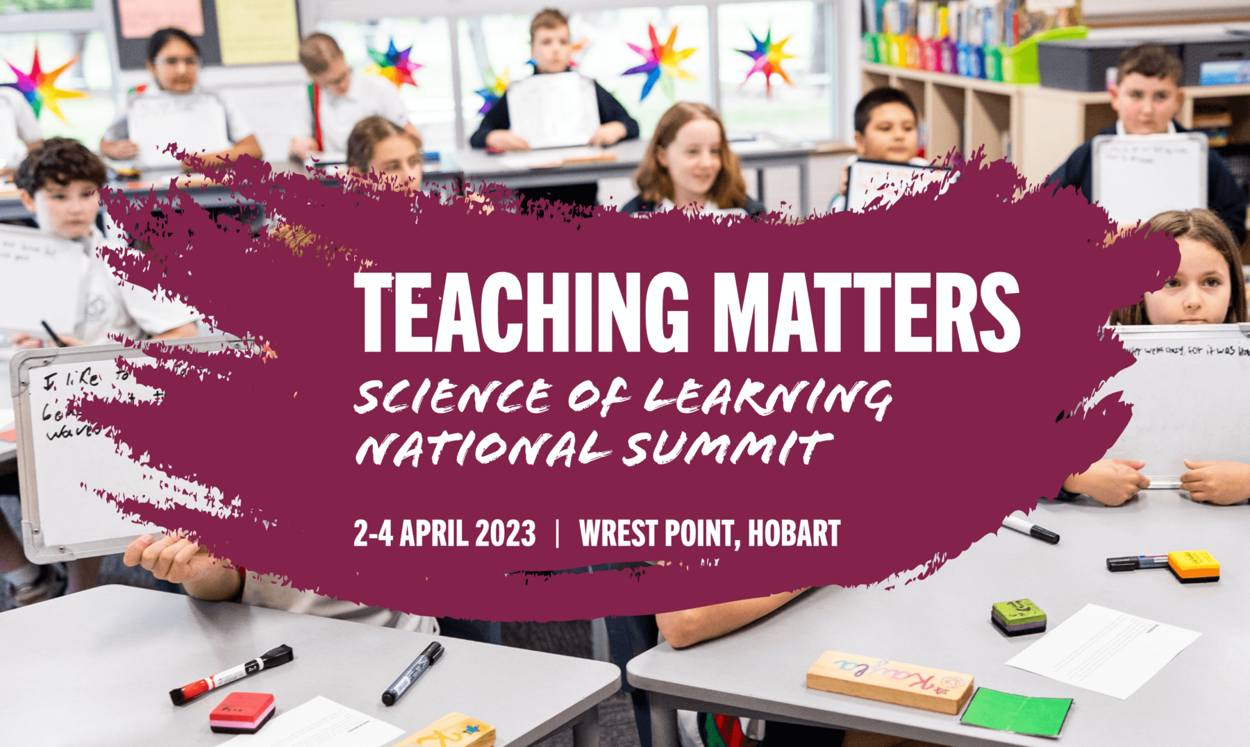 A promotional banner image with information about a conference shown in front of a classroom of younger children holding up pieces of paper.